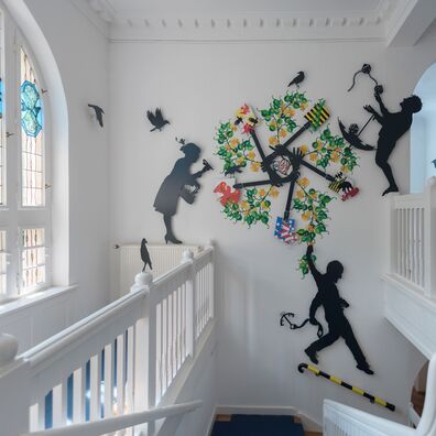 Ländernotarkasse Leipzig, Projekt Spectrum freies Notariat von Wolf v. Waldow – Treppenhauswand mit Emblem aus farbig bemaltem, gelasertem Stahlblech mit Wappen der 5 Neuen Bundesländer und Pflanzenzweigen; 3 Figuren die Aufgaben der Kasse illustrieren..