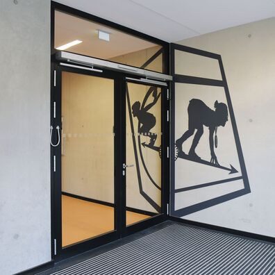 Foyer Sporthalle Kniprodestr. Projekt Hlifestellung – scherenschnittartige Figur aus Stahl auf Wand von Wolf v. Waldow, Motiv: Sportler in Startposition für Sprint, gegeüber sSportler in Startposition losfliegen.