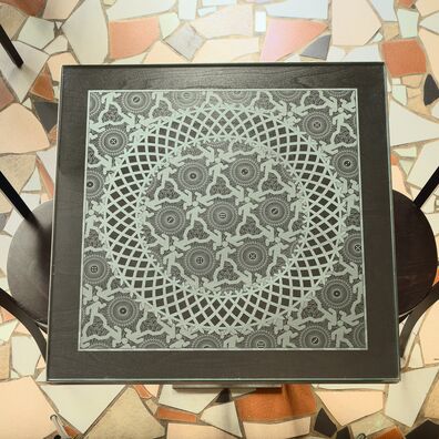 Café Bierhimmel: Tischplatte aus lasergraviertem Glas auf schwarzer Unterplatte; Motiv: Ornament aus laufender Figur Piktogramm "Notausgang", Würfeln und guillocheartigen Kreisformen