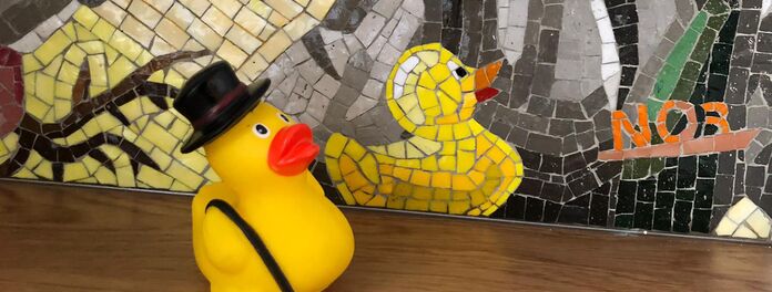 Ausschnitt Mosaikfries in Badezimmer zum Thema "Wasser als Ressource" von Wolf v. Waldow, Motiv: echte Gelbe Plastikente vor Mosaikdarstellung von gelber Plastikente; Hergestellt durch die Firma Cosmomusivo Berlin