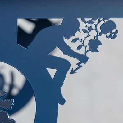 Tisch aus schwarz gepulvertem Stahl von Wolf v. Waldow; scherenschnittartige Figur sitzt zwischen Zarge und Tischbein, Motiv: Mann hält Zweig an dem angebissener Apfel und Apfel-Totenkopf hängt