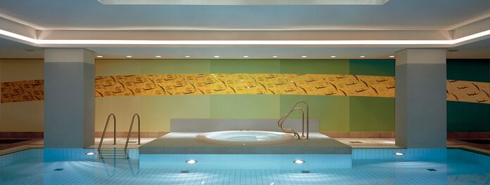 Schwimmbad Hotel Meridien Hamburg mit Wandarbeit H2O II von Wolf v. Waldow: Wasserbecken, Rückwand in Farbverlauf von hell- bis dunkelgrün, darauf gebogener, Streifen mit Ornament aus Kamelen in Gelb und aufgesetzen, polierten Stahlfiguren von Schwimmern