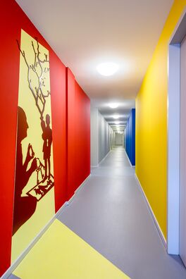 Flur im Lebensort Vielfalt Berlin mit Stahlarbeiten von Wolf v. Waldow: scherenschnittartige Figuren die einen Schattenriss vortäuschen, der aus einer gegenüberliegenden Tür auf die Wand zu fallen scheint.