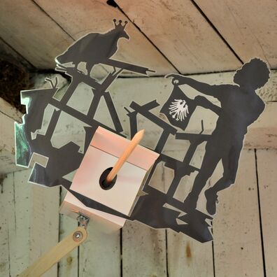 Projektraum "Hühnerhaus Volksdorf" mit Installation Neue Heimat von Wolf v. Waldow: Objekt in Form länglicher Überwachungs-Kamera, Front mit Motiv aus laminierten Papier: Migrant hält Tuch mit Deutschen Adler wie Torrero vor Ruine eines Gebäudes.