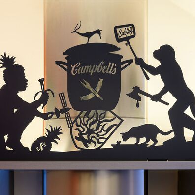Detail aus scherenschnittartigem Fries für Küche von Wolf v. Waldow; Motiv: Suppentopf mit "Campbell´s"-Schriftzug über heraldischem Feuer; Affe mit blutigem Beil und Handy, das Kalorien anzeigt; POC mit Knochen-Banane
