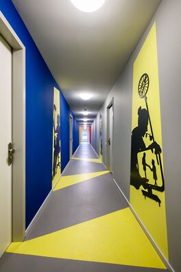 Flur im Lebensort Vielfalt Berlin mit Stahlarbeiten von Wolf v. Waldow: scherenschnittartige Figuren die einen Schattenriss vortäuschen, der aus einer gegenüberliegenden Tür auf die Wand zu fallen scheint.