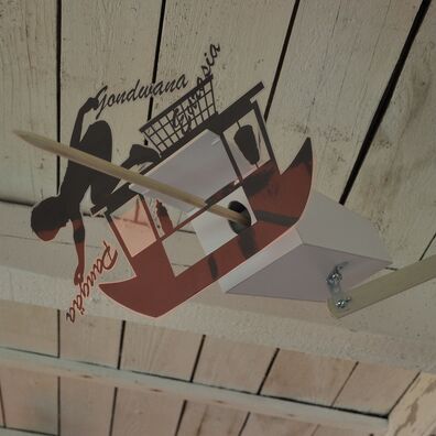 Projektraum "Hühnerhaus Volksdorf" mit Installation Neue Heimat von Wolf v. Waldow: Objekt in Form länglicher Überwachungs-Kamera, Front mit Motiv aus laminierten Papier das Schiffchen auf dem Junge mit Namen Gondwana und Pangäa in der Hand kniet zeigt.