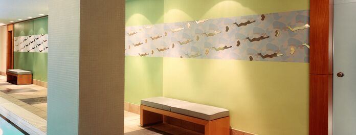 Schwimmbad Hotel Meridien Hamburg mit Wandarbeit H2O I von Wolf v. Waldow: Eingangswand in Farbverlauf von hell- bis dunkelgrün, darauf gerader Streifen mit Ornament aus Eisbären in blau und aufgesetzen, polierten Stahlfiguren von Schwimmern und Embryos