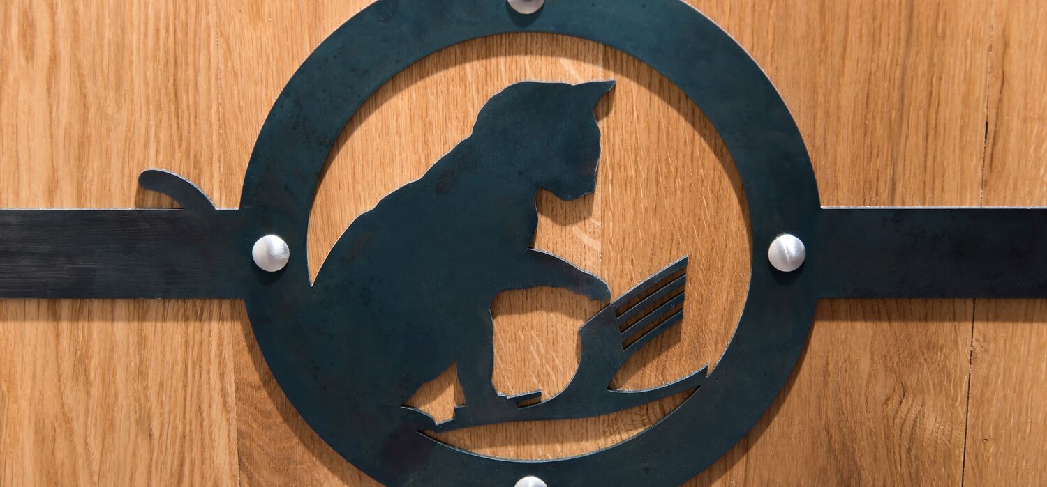 Metallbeschlag aus geschwärztem Stahl auf hölzerner Schranktür von Wolf v. Waldow; Motiv: Katze erlegt Lufthansa Kranich