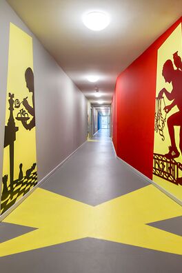 Flur im Lebensort Vielfalt Berlin mit Stahlarbeiten von Wolf v. Waldow: scherenschnittartige Figuren die einen Schattenriss vortäuschen, der aus einer gegenüberliegenden Tür auf die Wand zu fallen scheint.