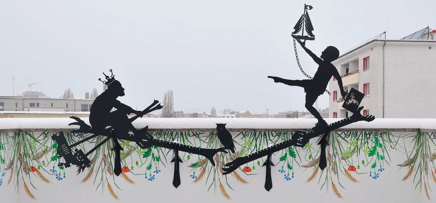 Balkon-Brüstung Berlin-Mitte mit Silhouetten-Arbeit von Wolf v. Waldow, Wand darunter mit Blumen bemalt, im Hintergrund Stadtpanorama Berlins; Motiv: junger Mann spaziert auf Lineal, gegenüber alter Mann sitzt rudernd auf zweitem Lineal