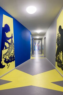 Flur im Lebensort Vielfalt Berlin mit Stahlarbeiten von Wolf v. Waldow: scherenschnittartige Figuren die einen Schattenriss vortäuschen, der aus einer gegenüberliegenden Tür auf die Wand zu fallen scheint.