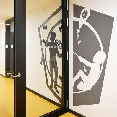 Rauchfangtür geschlossen Sporthalle Kniprodestr. Projekt Hlifestellung – 2 scherenschnittartige Figuren (1. Stahl, 2. gemalt) auf Wand von Wolf v. Waldow, Motiv: Sportler jongliert mit Hanteln, 2. Sportler versucht sie mit Tennisschläger zu treffen.